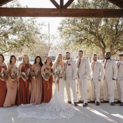 Wedding party group photo under rustic pavilion at Milagro Venue Texas, bridesmaids in terracotta and rust dresses
