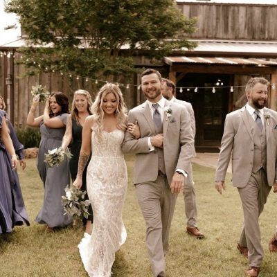 Wedding party walking across lawn with rustic barn in background at Milagro Venue Texas