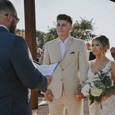 Bride and groom kissing under triangular wooden arch with pampas grass at outdoor boho wedding ceremony at Milagro Venue