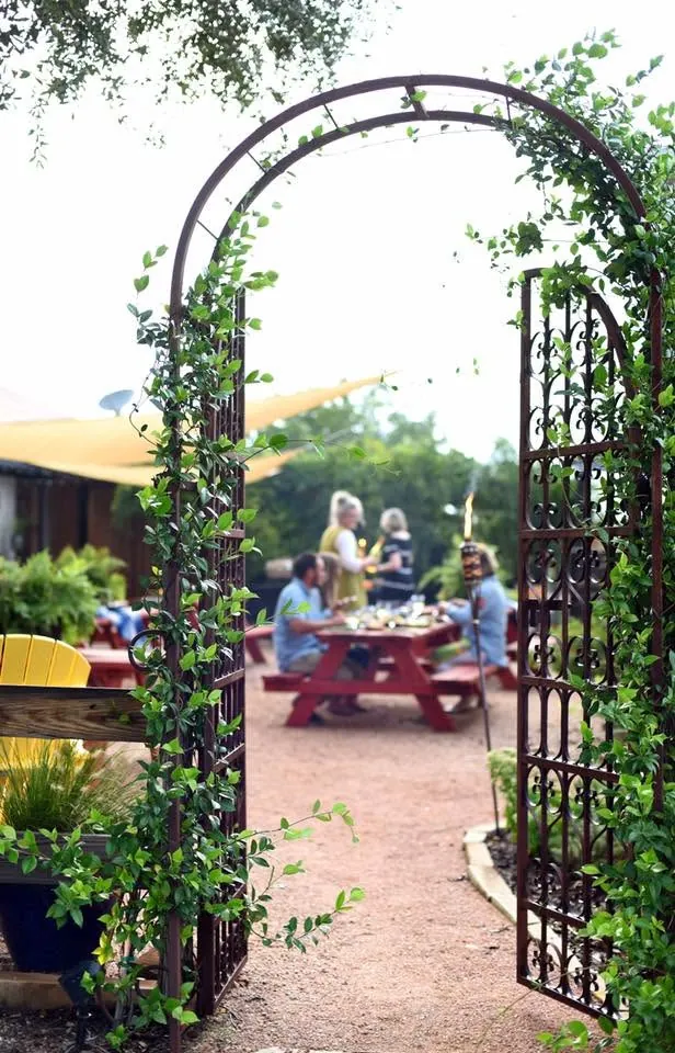 Wrought-iron garden arch covered in vines framing guests dining outdoors at Milagro Ranch Venue near Dallas, Texa