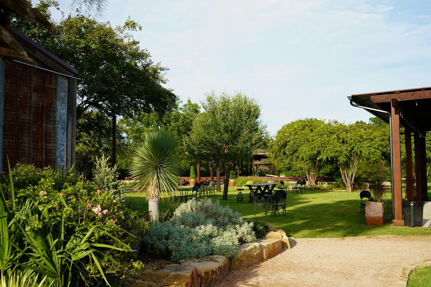 Landscaped garden lawn with bistro tables, string lights and covered pavilion at Milagro Ranch Venue in Forreston, TX
