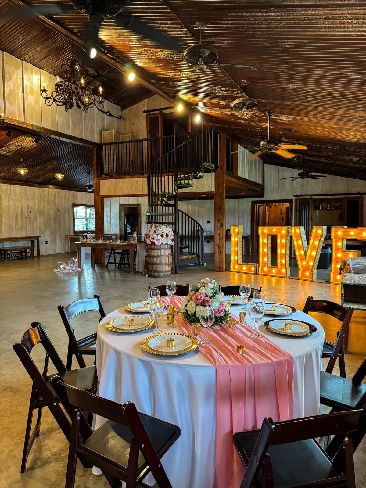 Rustic barn reception hall with spiral staircase, chandelier and lit LOVE marquee letters at Milagro Ranch Venue,